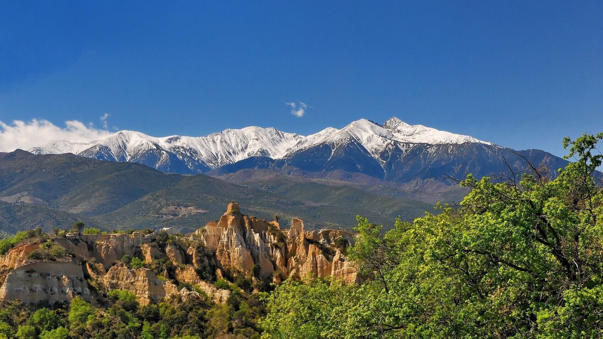 A mountainous landscape with snow-capped peaks, rocky formations, and green foliage.