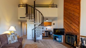 Amplia sala de estar con una escalera que conduce a un nivel superior, una chimenea y una cocina al fondo.