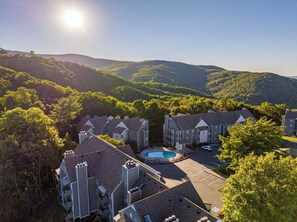 A residential complex with multiple two-story buildings, a central swimming pool, and surrounding lush greenery. - Ski View Summit • Pool, Hot Tub & Smoky Mtn Views (Gatlinburg)