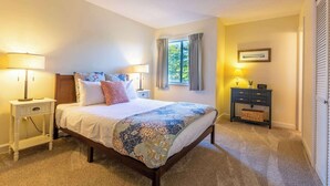 Un dormitorio con cama, dos mesitas de noche, una cómoda y un ventanal con cortinas.