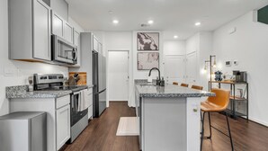 A modern kitchen with white cabinetry, stainless steel appliances, and a granite countertop. - Enjoyable 3-bedroom house with Firepit + Safe in charming Roseville (Roseville)
