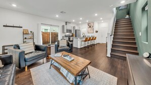 A modern living room with a wooden coffee table, a sofa, and a dining area with a kitchen in the background. - Enjoyable 3-bedroom house with Firepit + Safe in charming Roseville (Roseville)