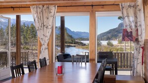 Ein Holzespeisetisch mit Stühlen, eine rote Kerze und Blick auf einen Fluss und Berge durch große Fenster.