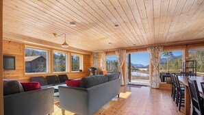 Ein großzügiger Wohnbereich mit Holzböden und -wänden, großen Fenstern mit Blick auf die Berge, einer Couch und einem Esstisch mit Stühlen.
