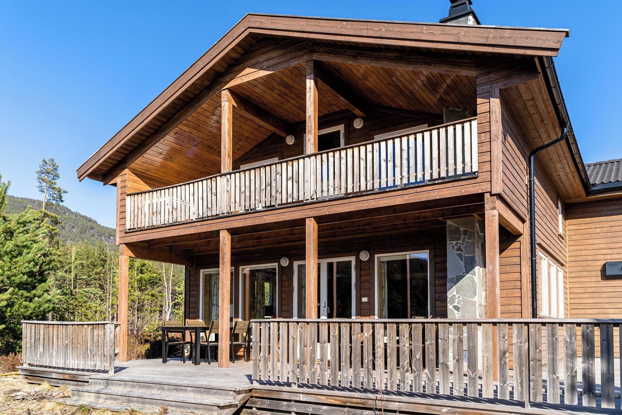 A wooden cabin with a balcony, large windows, and a stone accent wall.