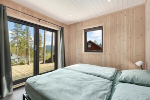 Une chambre avec une grande porte-fenêtre coulissante donnant sur une terrasse, une petite fenêtre et une lampe de chevet.