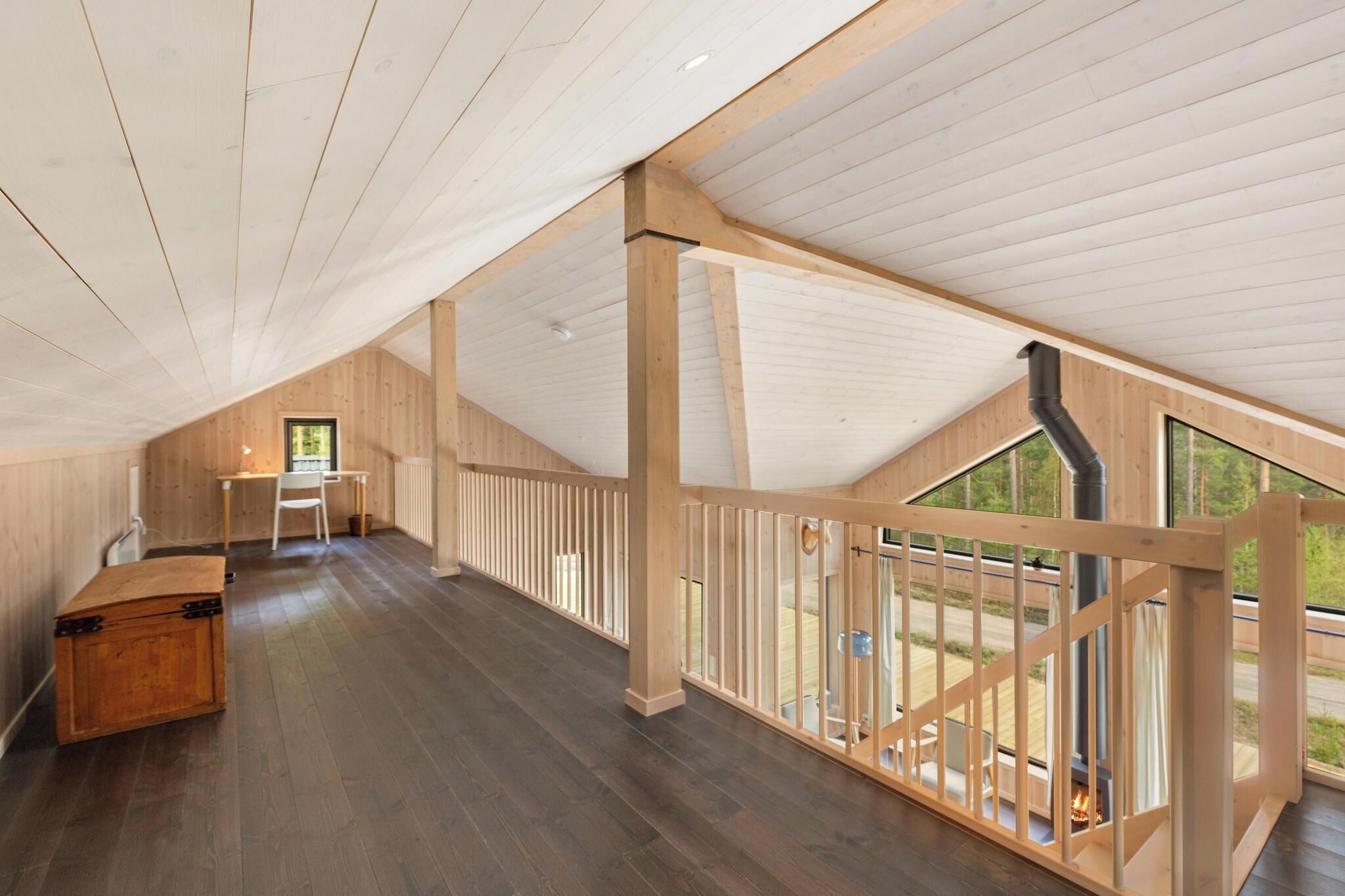 A spacious attic room with a high ceiling, wooden beams, a desk, and a view through a glass railing.