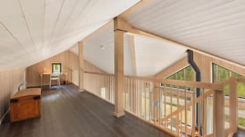 A spacious attic room with a high ceiling, wooden beams, a desk, and a view through a glass railing.