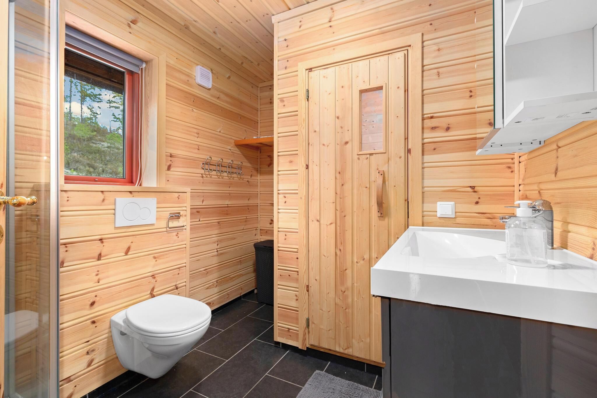 Un baño pequeño de madera con inodoro, lavamanos y ventana.