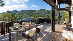 A wooden deck with a table set for dining, overlooking a mountainous landscape and a body of water.