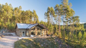 En stuga med ett tak av metall, stora fönster och en veranda med utomhusmöbler.