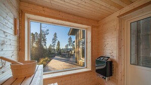 En stuga av trä med bastu, en träbänk och utsikt över en terrass och träd.