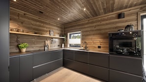 Cocina moderna con paneles de madera, horno empotrado y ventana que proporciona luz natural.