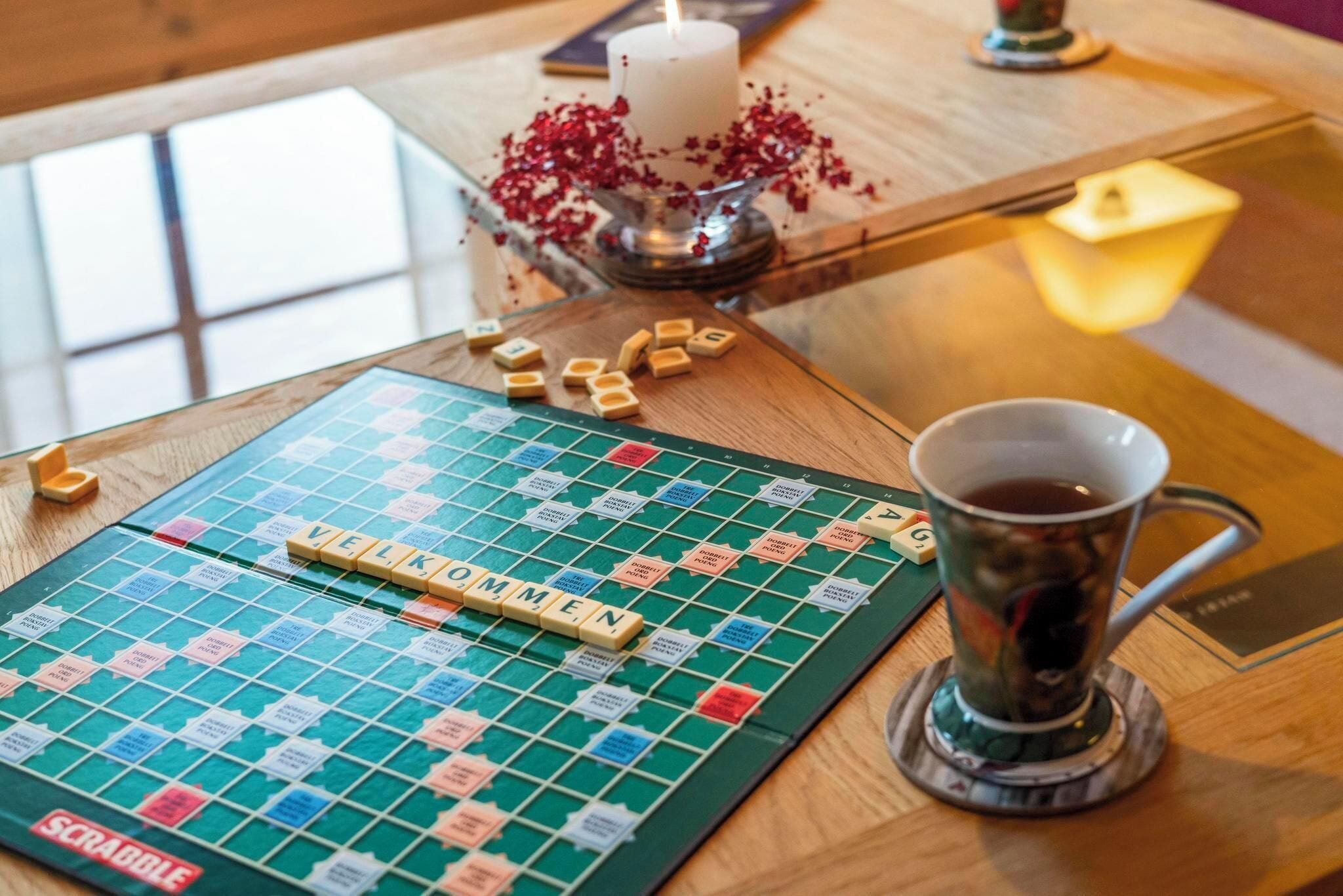 A Scrabble board game with tiles and a cup of tea on a wooden table.