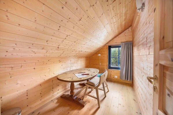 Una cabaña de madera con una mesa de comedor y sillas, una ventana con cortinas y una puerta.