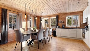 A modern kitchen with wooden cabinets, a dining area with a table and chairs, and large windows providing natural light. - Verhøf Hytte 9p - Four Bedroom Chalet, Sleeps 9 (Vrådal)