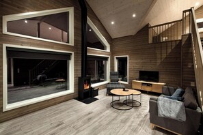 A modern living room with a fireplace, large windows, a staircase, and a TV. - Ivar Hytte 6p - Three Bedroom Chalet, Sleeps 6 (Vrådal)