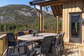 En træterrasse med et rundt bord og stole, med udsigt over et bjergrigt landskab.