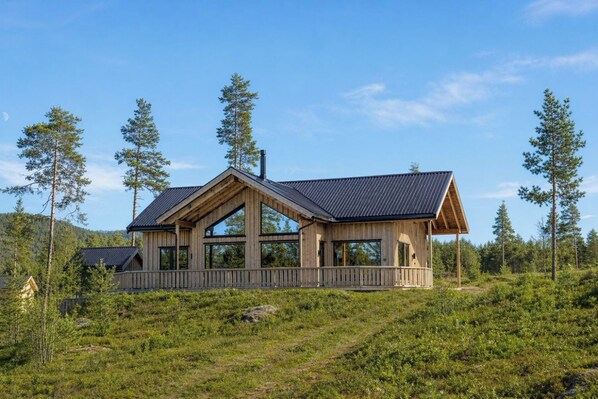 En træhytte med stor veranda, omgivet af høje træer og græslandskab.