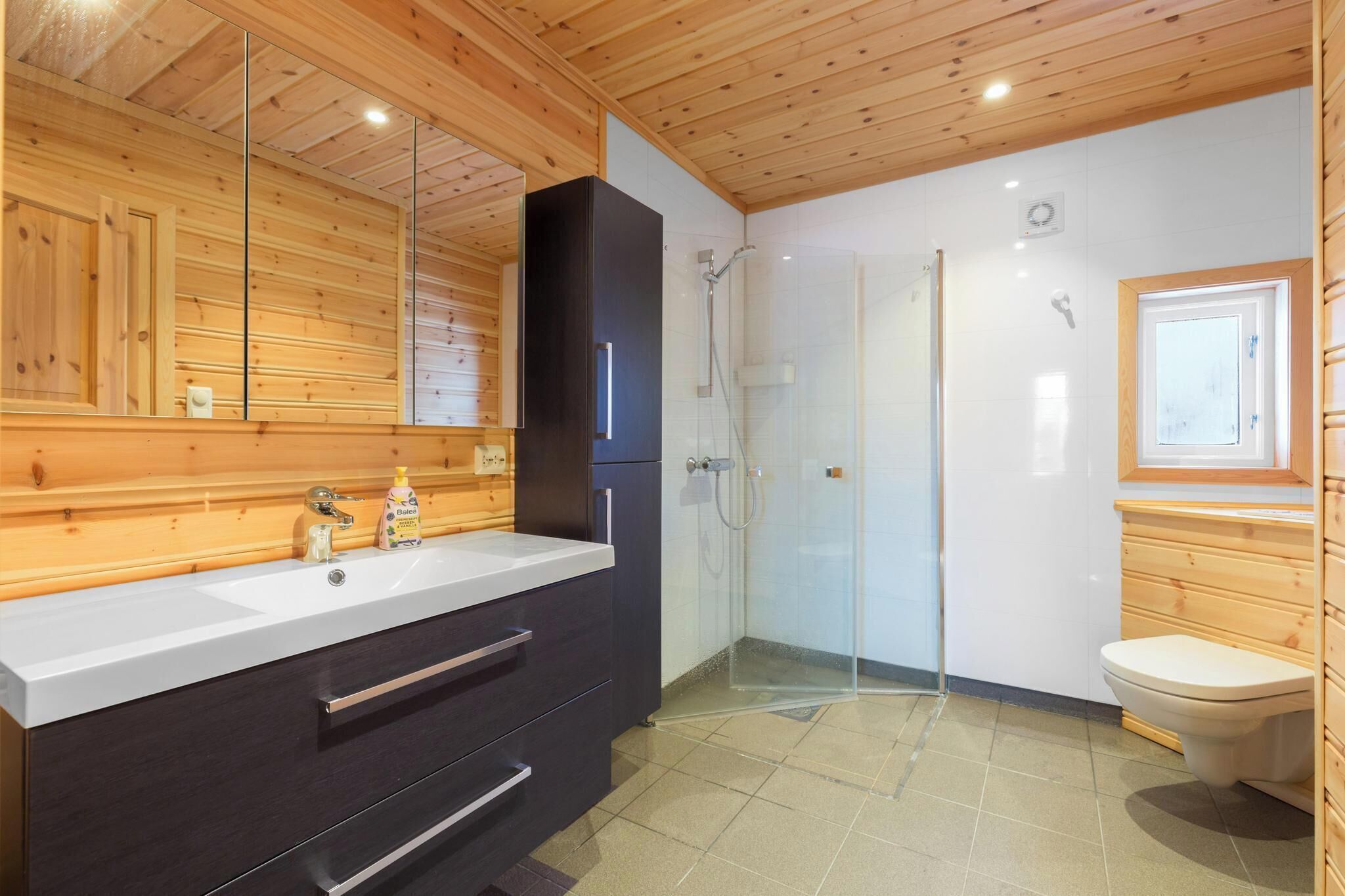 Ein modernes Badezimmer mit Holzboden, einem großen Spiegel, einem schwarzen Schrank, einer Duschkabine aus Glas und einer Toilette.