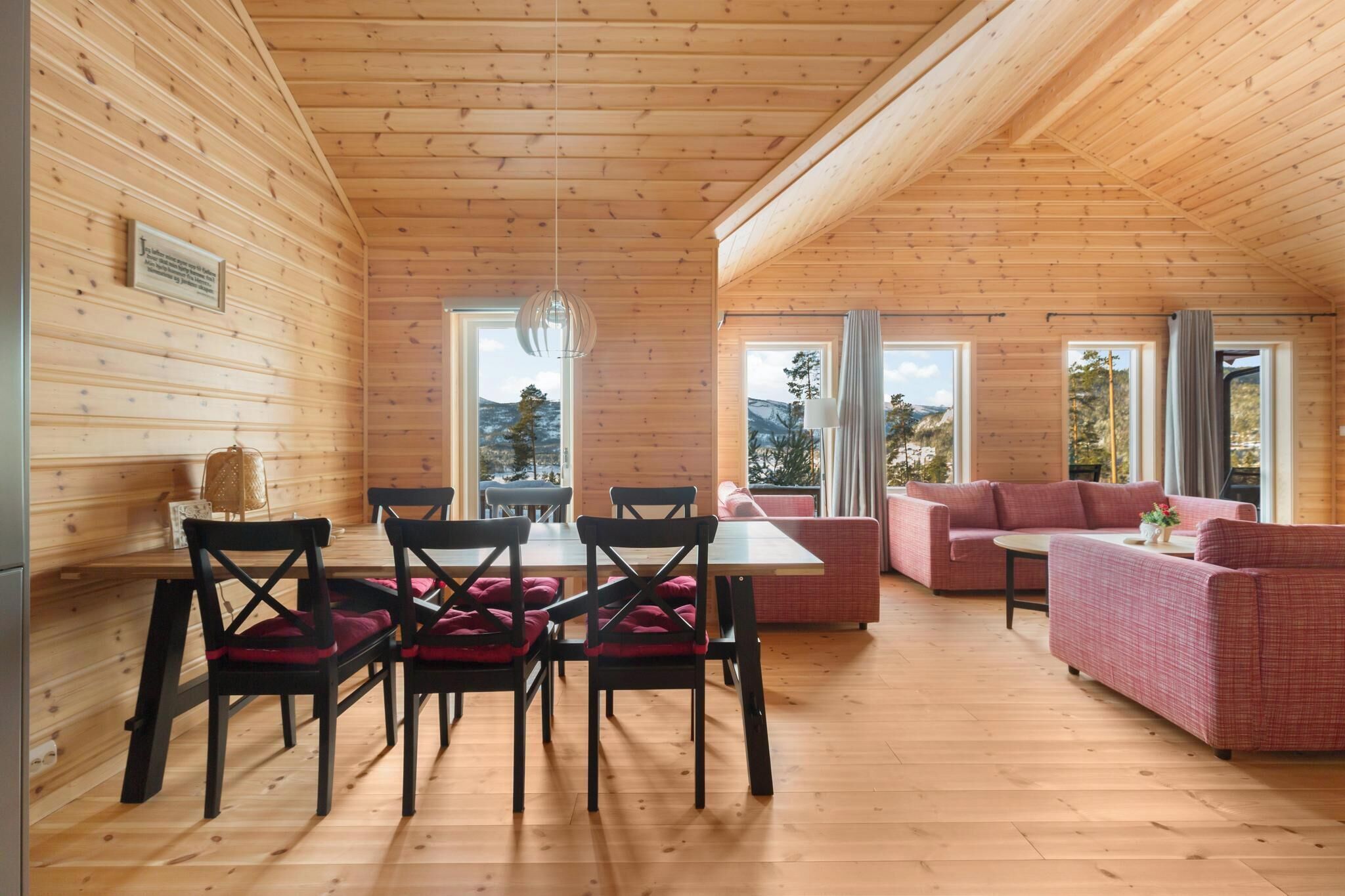 Un interior de madera con comedor, sofás y grandes ventanales que ofrecen vistas al exterior.