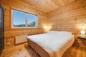 A wooden-paneled bedroom with a large window, a bed, a bedside table with a lamp, and a radiator. - Furuhus 8p - Four Bedroom Chalet, Sleeps 8 (Vrådal)