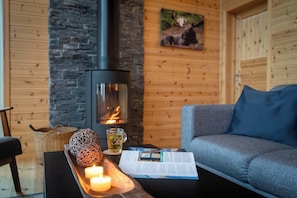 Ett mysigt rum med en stenmur, en öppen spis, en soffa, ett brickbord med ljus och ett glas te.