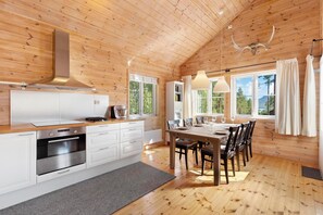 A wooden interior with a kitchen and dining area, featuring a large window, a hanging light fixture, and a ceiling-mounted light. - Chalet Vrådal 8p - Three Bedroom Chalet, Sleeps 8 (Vrådal)