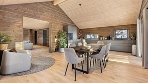 Un interior moderno con techo de madera, un comedor con una mesa y sillas redondas, una cocina con armarios grises y una sala de estar con sofá y planta en maceta.