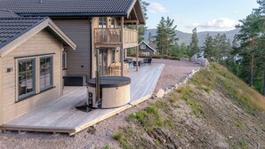Una cabaña de madera con terraza, jacuzzi y vistas a montañas y árboles.