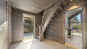 Un intérieur moderne avec un escalier en bois, une porte vitrée donnant sur l’extérieur et un espace cuisine visible à travers le verre.
