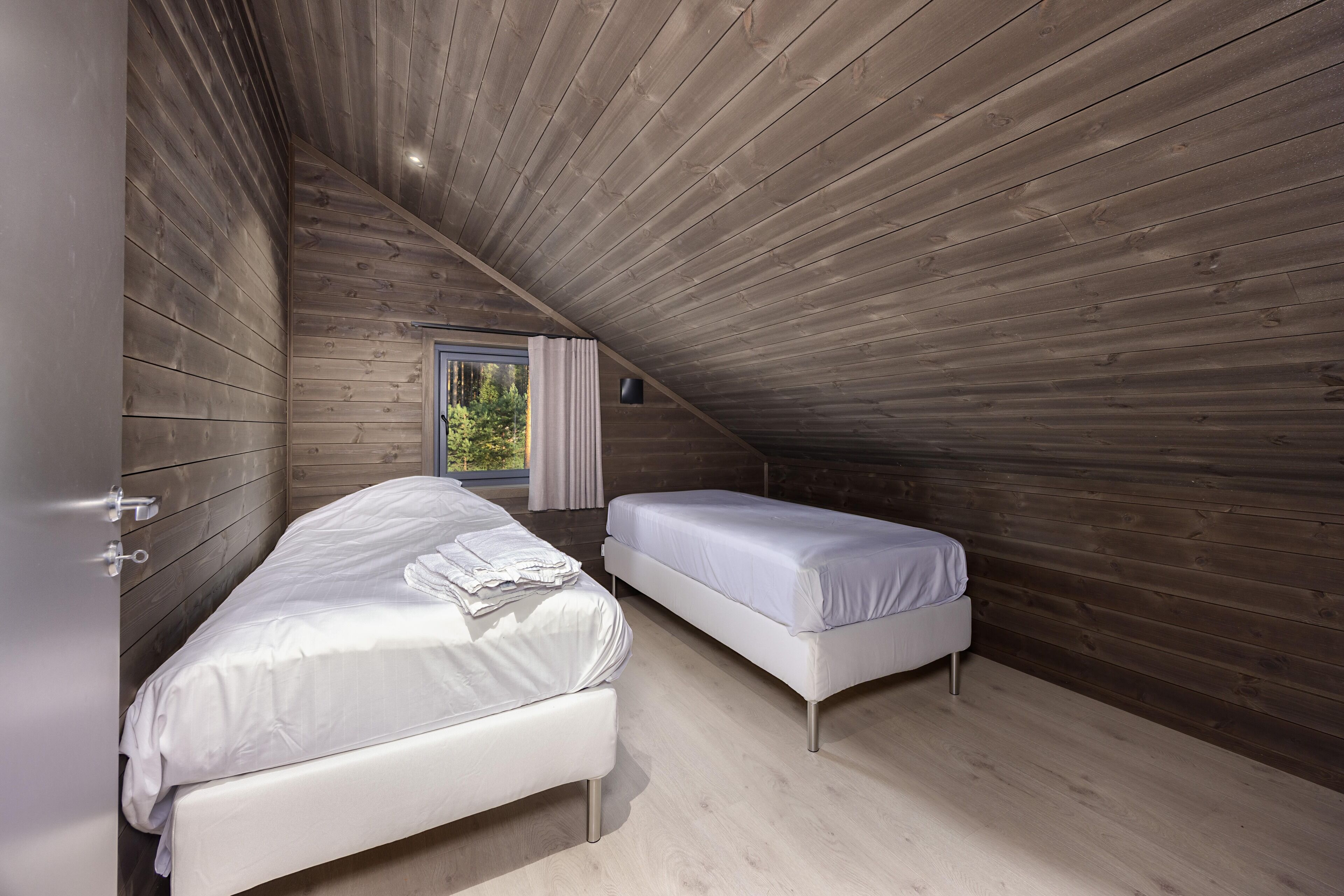 Een slaapkamer met twee bedden, houten wanden, een raam met gordijnen en een plafondlamp.