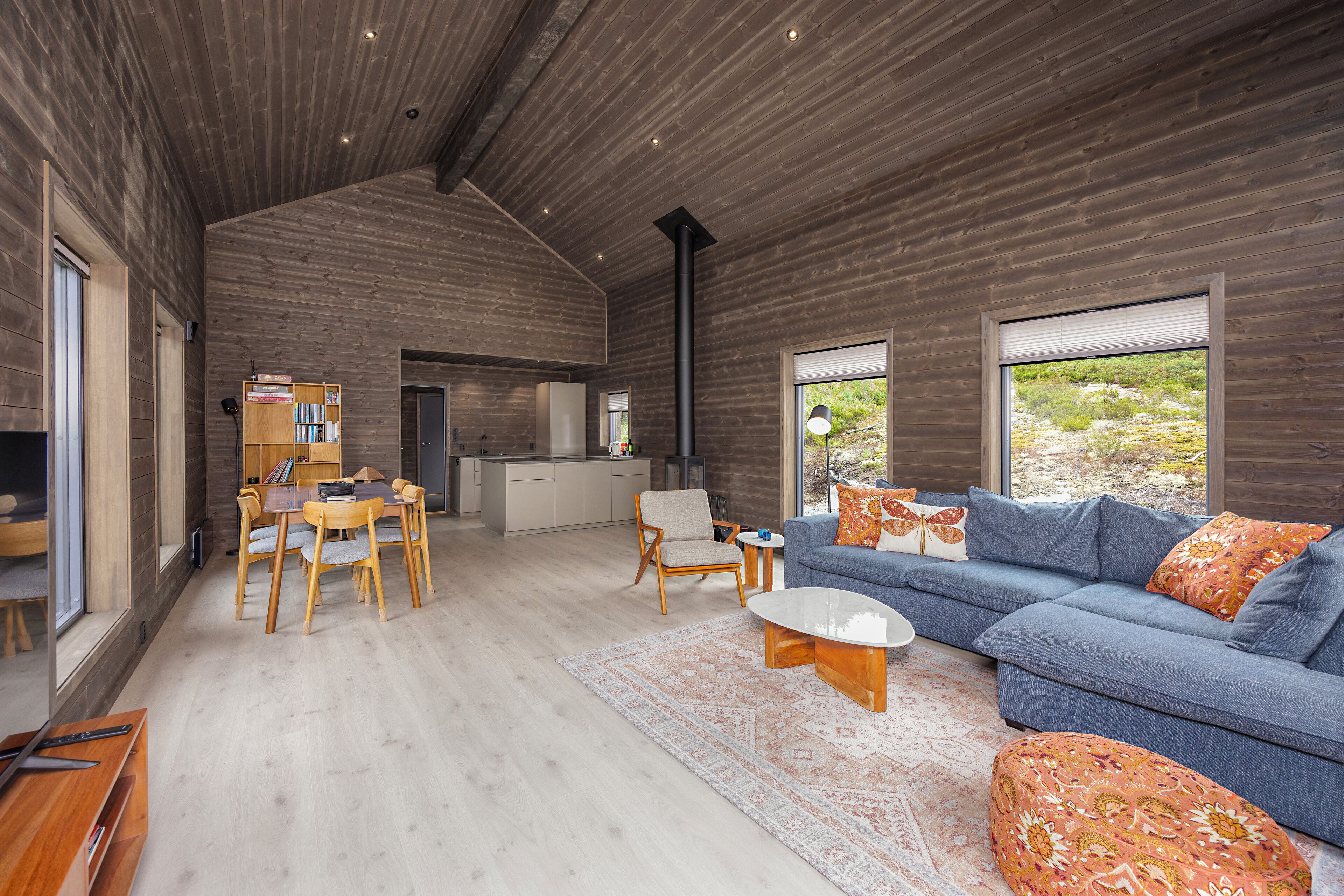 A modern interior with a wooden ceiling, a blue sofa, a wooden coffee table, and a dining area with chairs and a table.