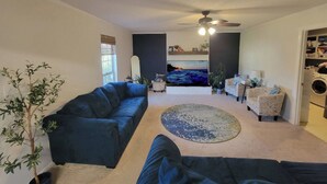 A living room with a dark blue sofa, a round rug, a ceiling fan, and a television. - Charming 3-bedroom house ready for the Masters (Martinez)