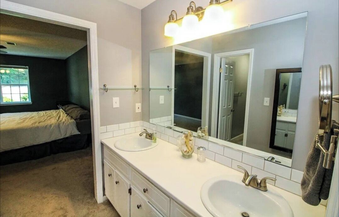 Un dormitorio con cama, un baño con dos lavamanos, un espejo grande y una ventana.