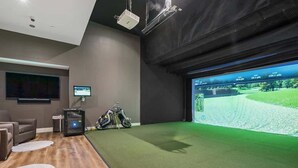 A room with a large screen displaying a golf course, a projector, a motorcycle, and a seating area. - Downtown Retreat w/ Pool, Hot Tub & Fire Pit (Louisville)