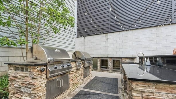 An outdoor kitchen area with a stone barbecue station, a sink, and a grill. - Downtown Retreat w/ Pool, Hot Tub & Fire Pit (Louisville)