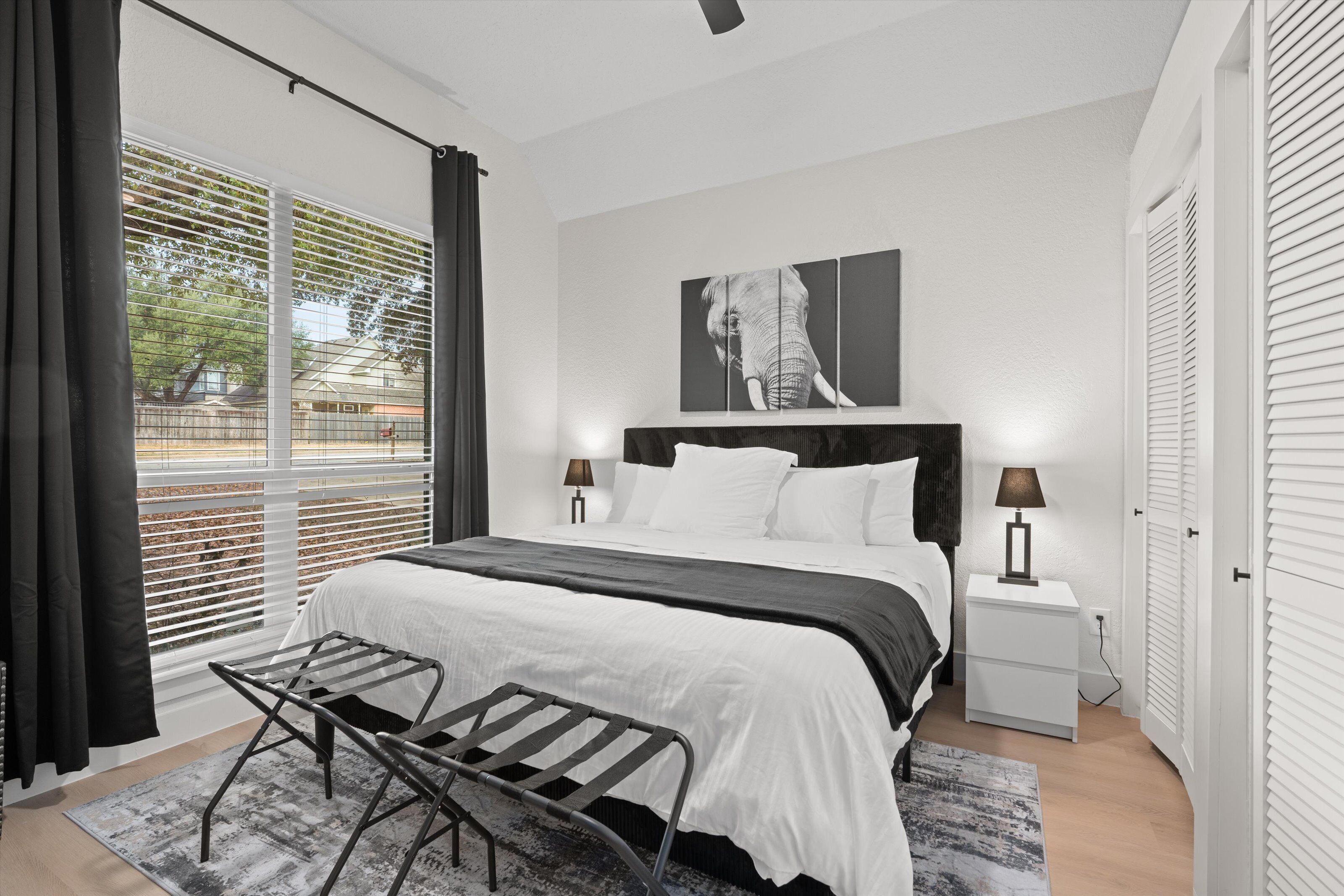 Une chambre à coucher moderne avec un grand lit, une table de chevet, un banc et une fenêtre avec des stores.