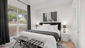 Une chambre à coucher moderne avec un grand lit, une table de chevet, un banc et une fenêtre avec des stores.
