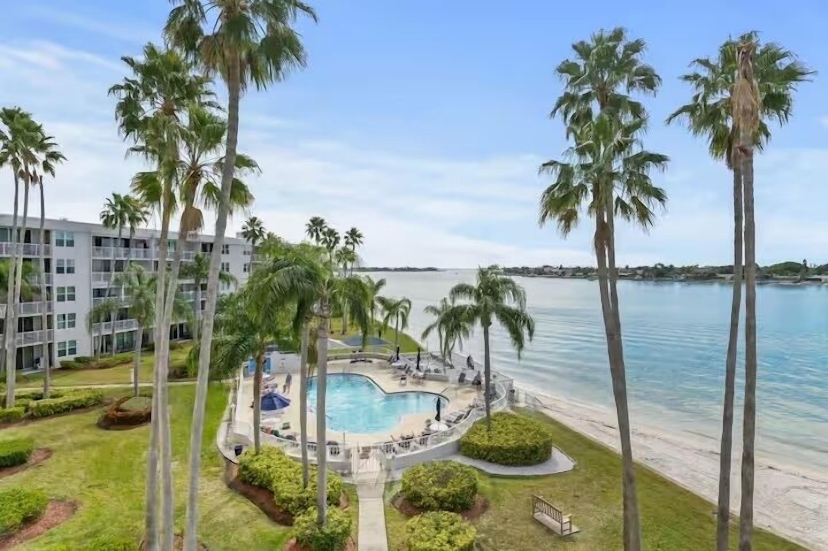A resort with a swimming pool surrounded by palm trees and a view of the ocean.