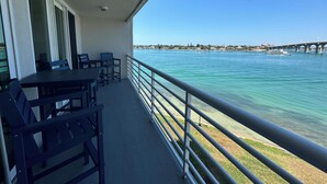 Ein Balkon mit Tisch und Stühlen, mit Blick auf ein klares blaues Meer, mit einer Brücke und Gebäuden in der Ferne.