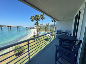 A balcony with a view of a beach, palm trees, and a bridge.