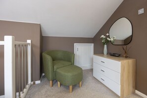 Ein Zimmer mit einem grünen Sessel, einem weißen Schminktisch, einem Spiegel und einer Tür.