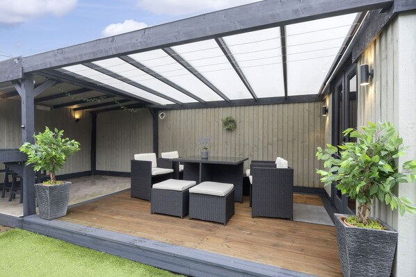 Eine Terrasse im Freien mit überdachter Sitzgelegenheit, einem Holzboden und Blumentöpfen.