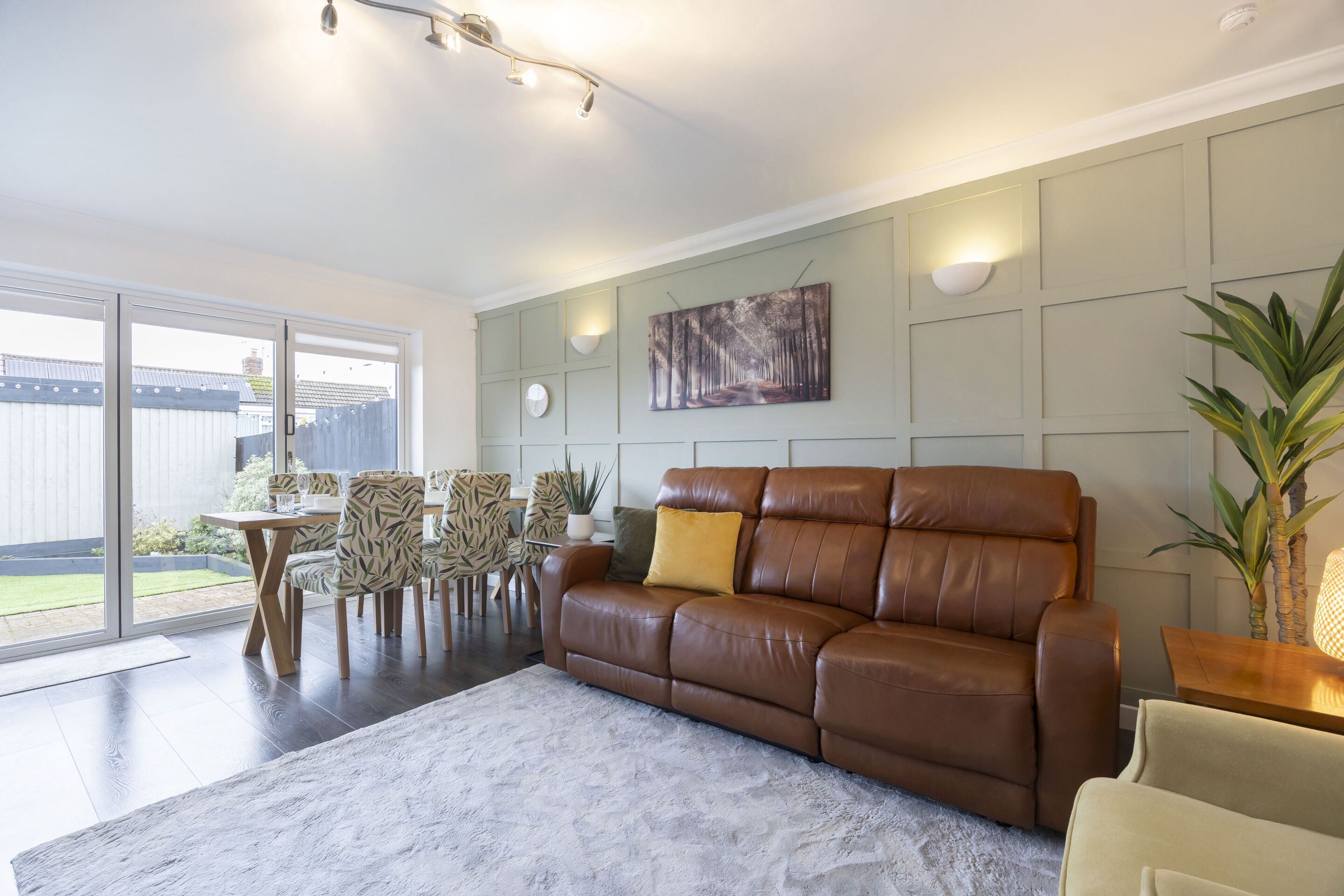 Een moderne woonkamer met een bruine leren bank, een eettafel met stoelen en een groot raam.