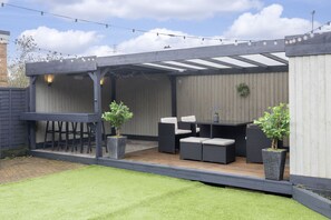 Eine Terrasse im Freien mit Holzdeck, Gartenmöbeln und Blumentöpfen.