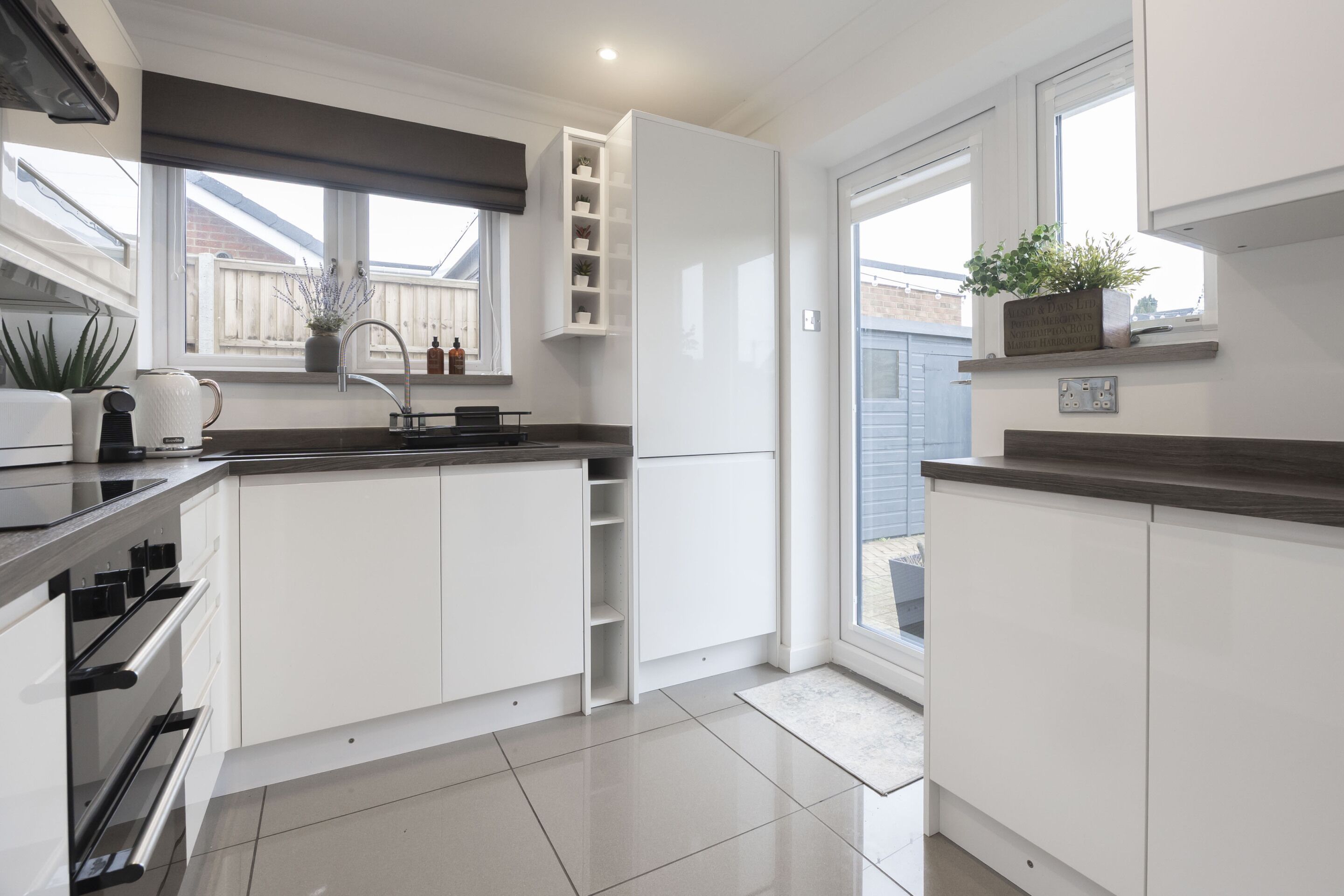 Una cocina moderna con armarios blancos, horno empotrado y ventana con vistas al jardín trasero.