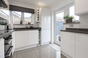 Eine moderne Küche mit weißen Schränken, einem Einbauofen und einem Fenster mit Blick zum Garten.