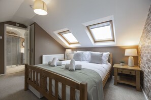 Ein Schlafzimmer mit schrägverdachter Decke, Dachfenstern, einem hölzernen Bett, einem Nachttisch mit Lampe und einer Ziegelwand.