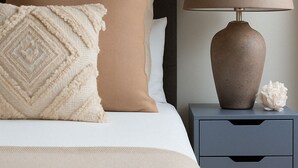 A neatly made bed with beige bedding, a matching throw blanket, and a decorative pillow. A bedside table with a lamp and a small decorative item is also visible. - Luxury Studios | E8 4DN | Balcony (London)